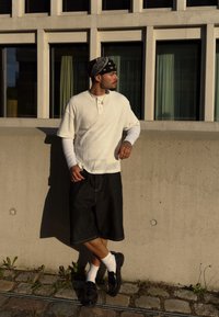 Bijela, rebrasta majica kratkih rukava s ovratnikom. Crne traper kratke hlače, bijele čarape i crne cipele bez vezivanja. Bandana naglašava look.