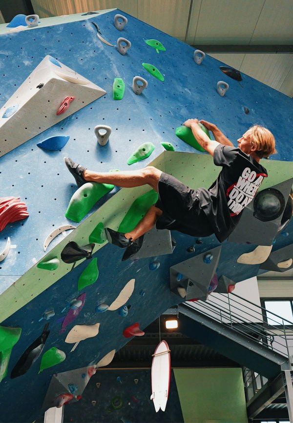 Young climber grips green holds on an indoor overhanging climbing wall with various colored handholds and footholds.