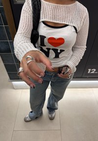 Valge kudum, avatud kaelusega särk sobitatud tiheda "I ❤️ NY" särgiga. Sinised laiad püksid ja hallid jalanõud. Hõbedased sõrmused sõrmedel.