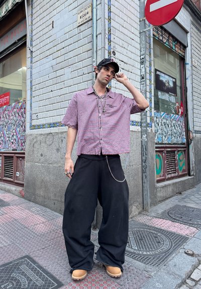 Camisa de manga corta a cuadros en rojo y blanco combinada con pantalones anchos negros y zuecos color beige, complementada con una cadena de plata.