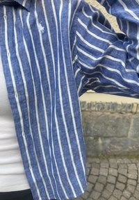 Camisa de linho riscada em azul e branco com frente abotoada e bordado de logótipo. Apresenta mangas largas e uma textura de ajuste relaxado.