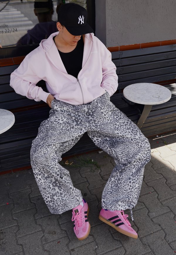 Svijetlo ružičasti dukserica na zip, crna majica, sivi hlače sa leopard printom, i ružičaste tenisice s crnim prugama, sjedi pored mramornog stola.