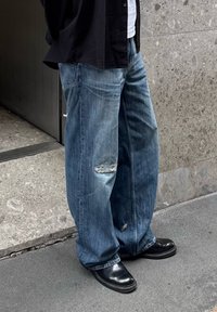 Volné modré džíny z denimu s ošoupaným vzhledem a roztrženým kolenem, spárované s černými koženými botami. Design má uvolněný střih.