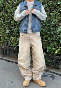 Farmernadrág mellény, szürke pulóver, bézs bársony nadrág és bézs csizma. Az öltözet laza szabású, texturált anyagokkal és rétegezett stílussal.