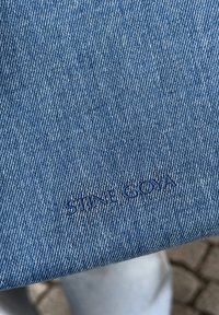 Μπλε τζιν ύφασμα με υφή. Φέρει ανάγλυφα γράμματα "STINE GOYA" σε πιο σκούρο μπλε. Απλός και καθαρός σχεδιασμός.