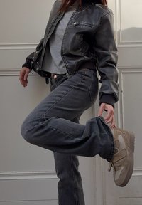 Čierna kožená bomber bunda, šedé tričko, šedé denimové nohavice, béžové tenisky. Funkcie zahŕňajú rebrované manžety, zipsové vrecká a voľný strih.