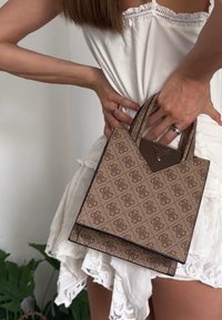 Borsa a tracolla marrone con motivo, superficie testurizzata, doppi manici e un accento a forma di triangolo sul lato superiore. Forma rettangolare compatta.