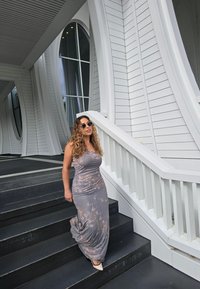 Dlhé priliehavé sivé šaty s jemným vzorom tie-dye. Oblečené s okrúhlymi slnečnými okuliarmi a opätkami so špicatými špičkami, na schodisku.