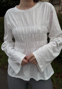 Λευκή μπλούζα με μακριά μανίκια που διαθέτει σμιλευτό σχέδιο στη μέση, με φαρδιά μανίκια και στρογγυλή λαιμόκοψη, φτιαγμένη από μαλακό ύφασμα.