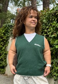 Grønn ermeløs genser med v-hals, ribbet tekstur og hvit bølget kant. Har en hvit "Dickies" logo på venstre side.