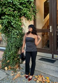 Dark grey strapless top with a fitted design, black skinny trousers, and burgundy high heels. Accessorised with a black faux fur clutch. Green ivy background.