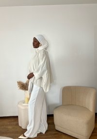 Bluză albă cu mâneci lungi și croială lejeră, asortată cu pantaloni largi albi. Un hijab alb și un accesoriu de păr auriu decorativ completează ținuta.