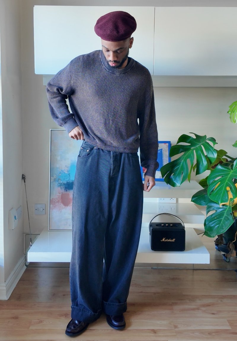 Dark blue wide-leg trousers and a textured dark gray sweater, paired with a maroon beret and black shoes, in a modern interior setting.