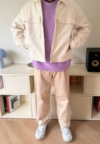 Kremfarget zip-up jakke, lilla strikkegenser, beige bukser og grå joggesko. Teksturerte materialer og avslappet passform med frontlommer.