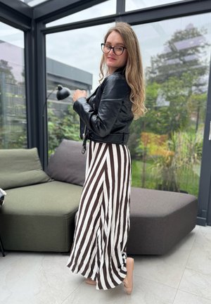 Chaqueta de cuero negra sobre una falda larga con rayas verticales en marrón y blanco. Tejido suave con un diseño fluido. Zapatos de color claro.