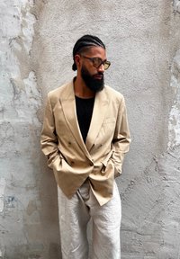 Blazer beige doppiopetto, tessuto strutturato, rever a punta, t-shirt nera sotto, abbinato a pantaloni in lino di colore chiaro.