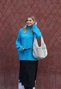 Nadmierny turkusowy wełniany sweter z prążkowanym dołem, zestawiony z czarną spódnicą ozdobioną koronkowym wykończeniem. Nosi białą torbę z ćwiekami.