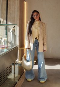 Beige oversized blazer, lys gul skjorte, vide lyseblå jeans og metallisk gull håndveske. Klare solbriller og platåsko.