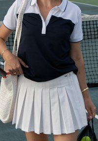 Polo shirt blu navy e bianco con colletto, abbinato a una gonna da tennis bianca plissettata. Presenta un tessuto testurizzato e un accento decorativo in vita.