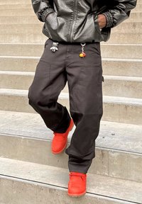 Czarne spodnie bojówki z wieloma kieszeniami, w połączeniu z jasnoczerwonymi butami. Do spodni przymocowane breloczki dodające koloru i detali. Tkanina o fakturze.