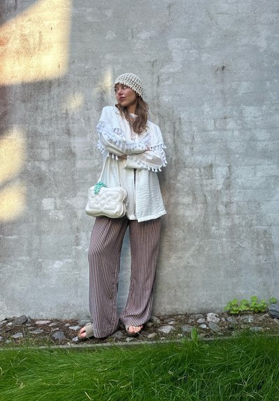 Top blanco texturizado con detalles de pompones, pantalones rayados en marrón claro y crema, y un bolso crema con herrajes en turquesa.