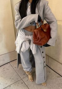 Grey oversized blazer over a matching grey crop top and joggers, paired with beige slouchy boots and a small brown handbag.