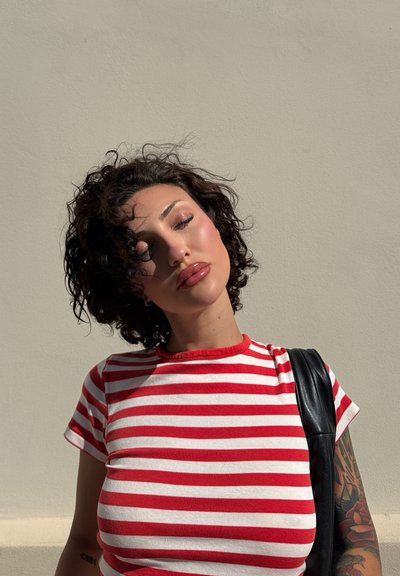 Camiseta de rayas rojas y blancas con mangas cortas, con un escote redondo. Un bolso negro descansa sobre el hombro, con un fondo texturizado.
