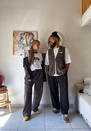 Pantalones y chaleco de estampado de leopardo, camiseta blanca y mangas largas transparentes negras. Zapatos amarillos y grises. Fondo neutro con una obra de arte texturada.