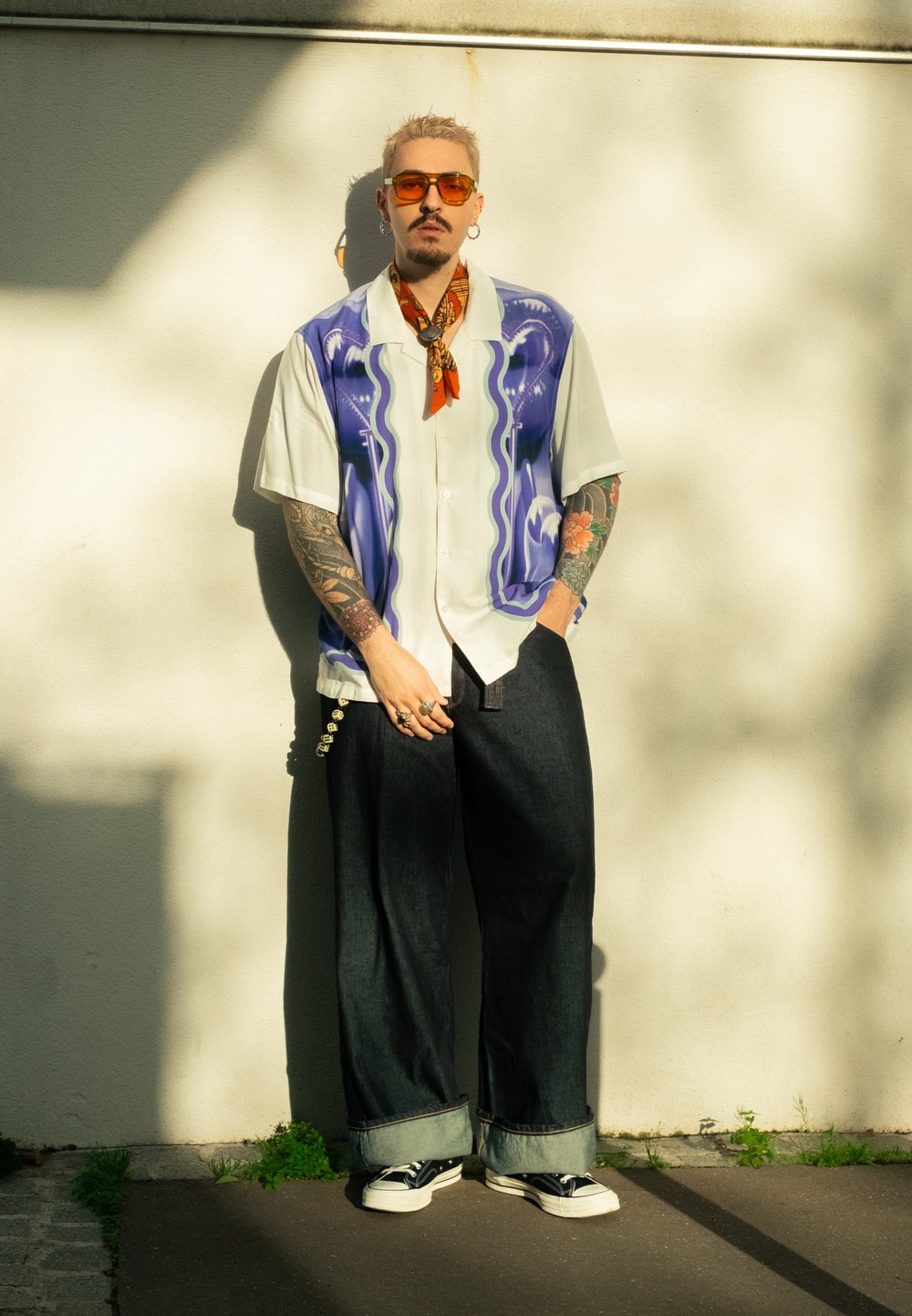 Košile s krátkým rukávem s bílým základem a modro-zeleným abstraktním vzorem. Kombinována s tmavými džínami, ohrnutými manžetami a černými teniskami.