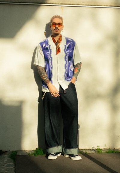 Camisa de manga corta con base blanca y un diseño abstracto en azul y verde. Combinada con vaqueros oscuros, puños doblados y zapatillas negras.