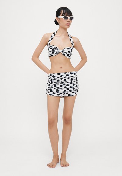 Bikini de lunares en blanco y negro con cuello halter, que presenta un diseño de frente retorcido y una falda con frunces a juego. Textura de tela suave.
