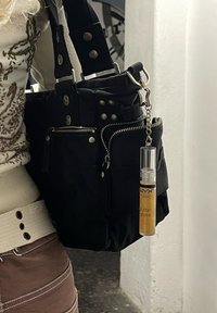 Svart tygväska med flera dragkedjefickor, silverfärgad detaljering och ett guld NYX butter gloss fäst med en kedja. Distinkt design.