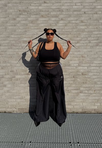 Conjunto atlético negro que incluye una camiseta sin mangas corta y pantalones de chándal sueltos con rayas laterales. Los accesorios incluyen un pequeño bolso negro y gafas de sol.