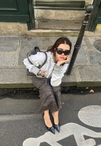 Grijze sweatshirt met geribbelde mouwen, gedragen over een lange rok met camouflagepatroon. Zwarte pumps met spitse neuzen en een gevlochten handtas met een kettinghengsel.