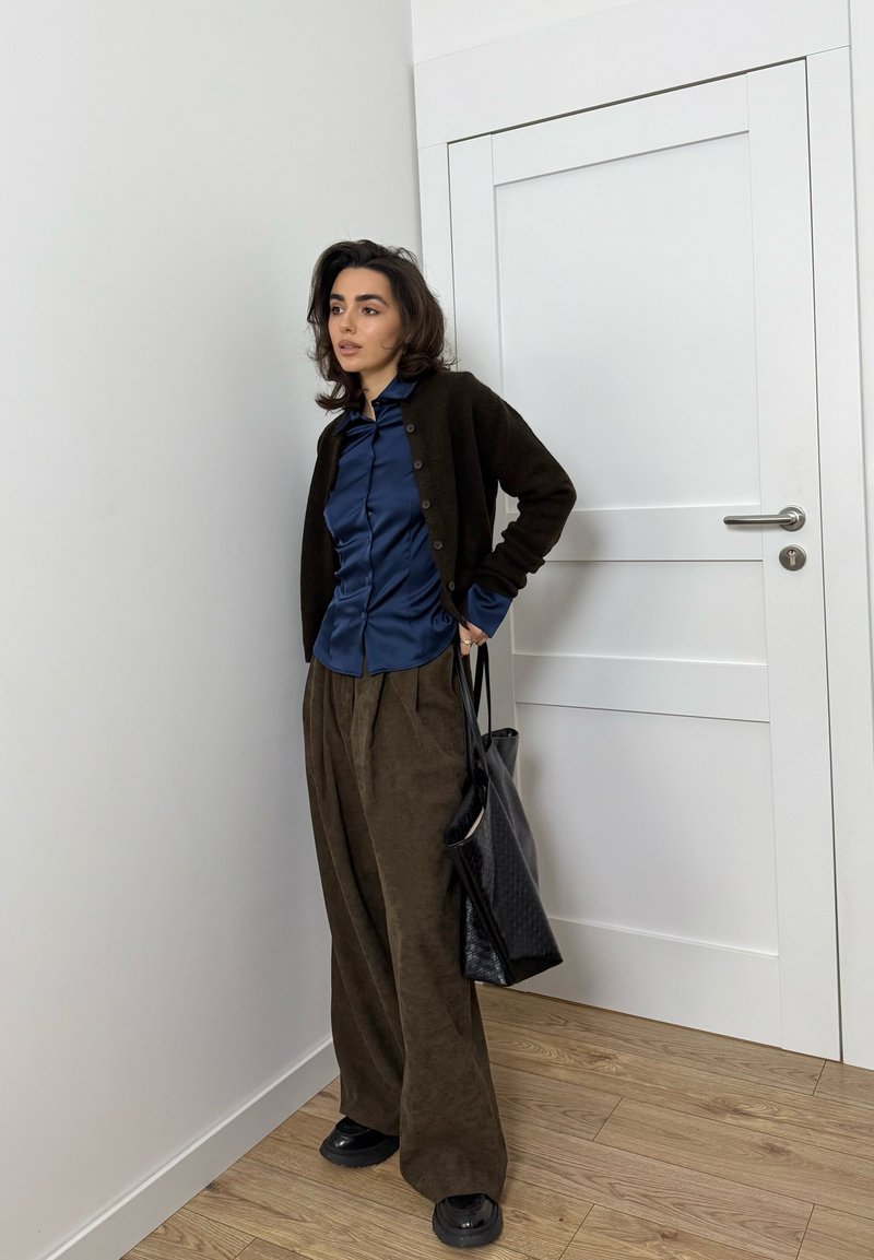 Black cardigan, navy satin shirt, brown wide-leg trousers, black bag, and chunky black shoes. Smooth textures and a relaxed fit.