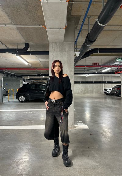 Suéter negro corto, culottes de mezclilla negros de talle alto, botas negras gruesas. El accesorio incluye un cinturón con una hebilla circular y una cadena de cuentas.