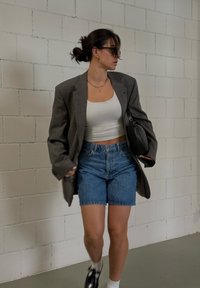 Γκρι �υπερμεγέθη σακάκι πάνω από λευκό crop top, συνδυασμένο με ψηλόμεσα τζιν σορτς. Η μαύρη τσάντα και τα μαύρα παπούτσια ολοκληρώνουν την εμφάνιση.