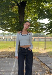 Dlhý rukáv, svetlosivý crop top s odkrytými ramenami, skombinovaný s čiernymi rifle s vysokým pásom a širokými nohavicami. Pozoruhodné čierne akcenty na výstrihu.