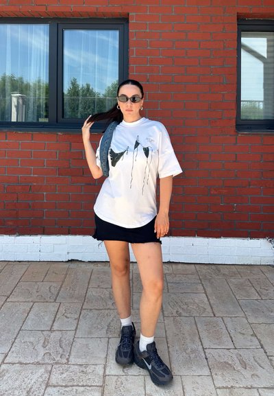 Camiseta gráfica blanca con dibujo negro, combinada con una falda de mezclilla negra. Zapatillas negras, calcetines blancos y un accesorio gris colgado del hombro.
