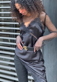 Sort satin kjole med blonderkant, lange gennemsigtige mesh-ærmer prydet med perler; kombineret med stribede bukser og et sort bælte med guldlås.