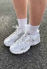 Adidași albi New Balance, confecționați din materiale din plasă și piele, cu modele punctate, tălpi texturate și accente reflectorizante.