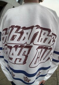 Λευκό πουκάμισο με μακριά μανίκια που διαθέτει έντονο μαρόν γραφικό κείμενο στην πλάτη, με μπλε ριγέ λεπτομέρειες στα μανίκια και ραμμένο υλικό.