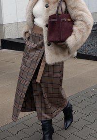 Gonna a portafoglio in plaid marrone abbinata a un maglione beige, un cappotto in pelliccia sintetica e una borsa in suede bordeaux. Stivaletti neri con punta appuntita completano l'outfit.