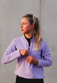 Light purple zip-up jacket with long sleeves, made of smooth fabric, featuring a white logo on the chest and a mock collar design.