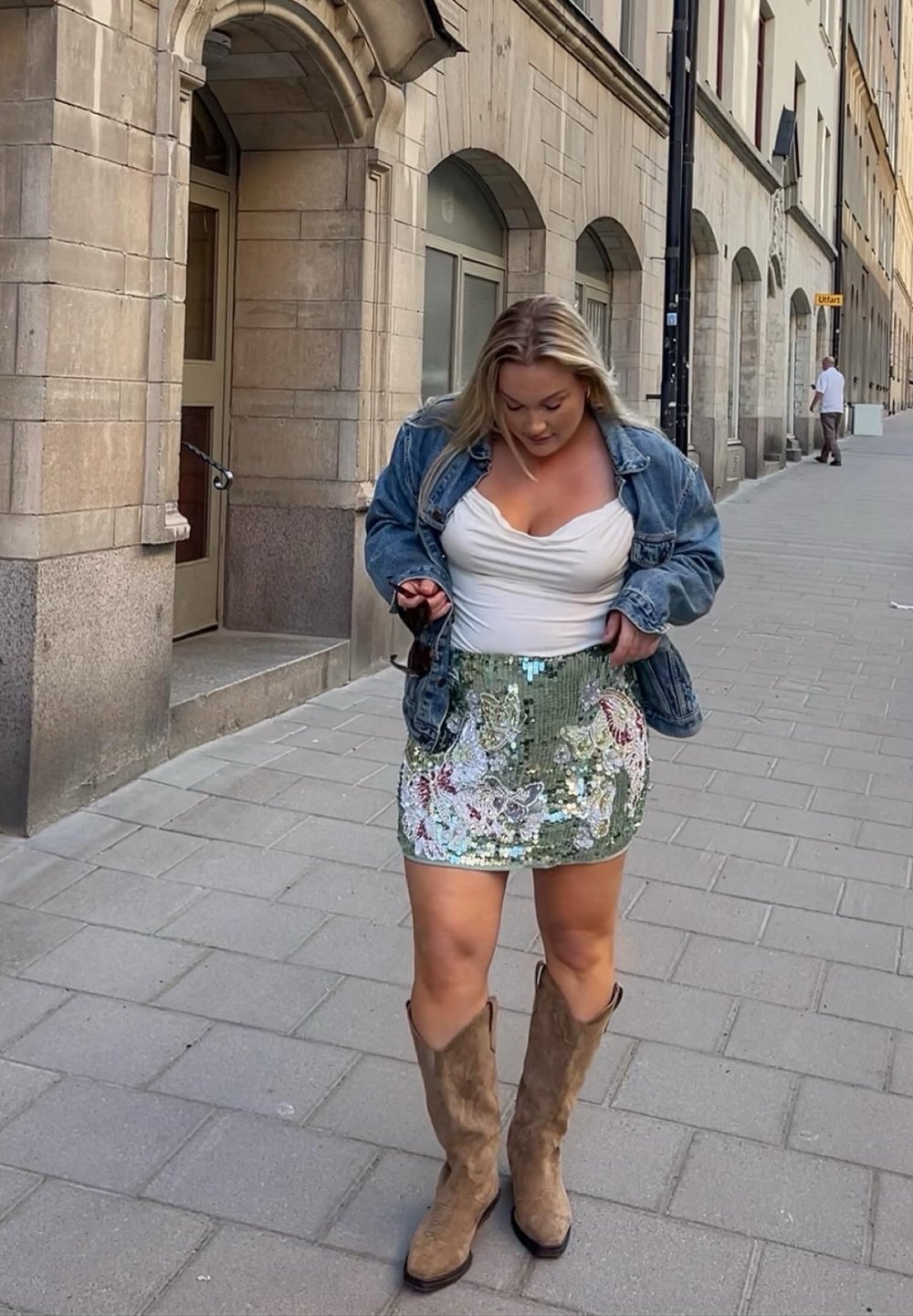 Zelena mini krila s sequinsami in cvetličnim vzorcem, kombinirana z belim oprijitim topom in svetlobluzim denim jakno. Rjave kavbojke čevlje.