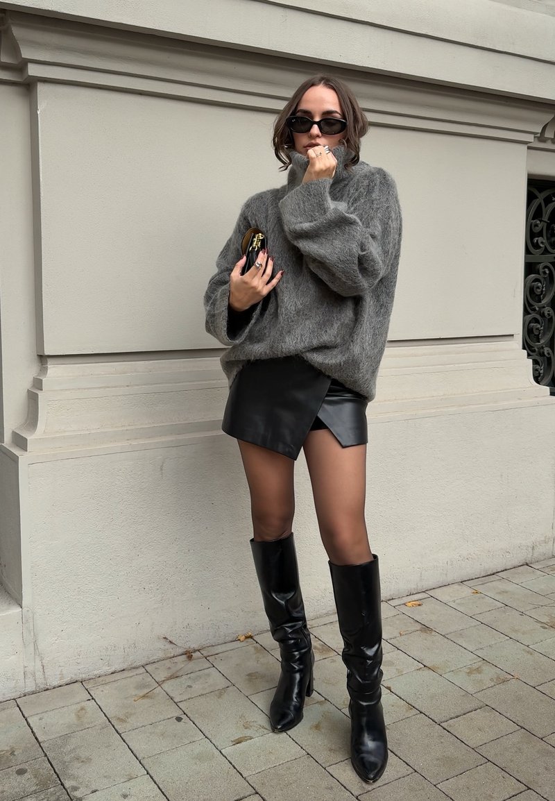 Pelēks pārāk liels džemperis, melna ādas mini svārki un melni augstpapēžu zābaki līdz ceļiem. Aksesuāri ietver saulesbrilles un mazu rokas somu. Strukturētas auduma.