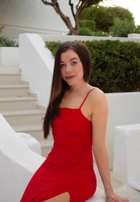 Red, sleeveless dress with a tailored fit and a side slit. Made from a smooth, stretchy fabric; positioned against white stone steps and lush greenery.
