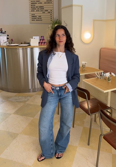 Jeans de pierna ancha en azul combinados con una camisa blanca ajustada y un blazer azul marino. Joyas de plata como acento con una camiseta a rayas debajo del blazer.