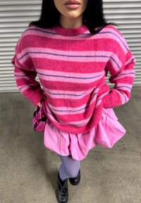 Suéter de malha às riscas cor-de-rosa e roxas com um decote alto, combinado com uma saia em camadas cor-de-rosa e meias roxas, usado com botas pretas.