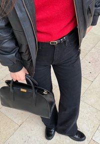 Άτομο που φοράει κόκκινο πουλόβερ, μαύρο δερμάτινο μπουφάν, μαύρη ζώνη και παντελόνι, μαύρα παπούτσια, κρατώντας μαύρη τσάντα σε πλακόστρωτο δάπεδο.